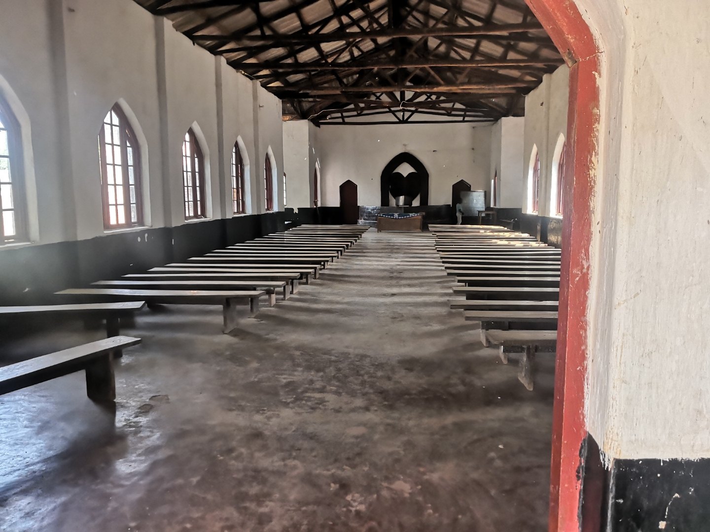 The interior of a rural Malawi church, rows of simple wooden benches leading to the altar beneath a timber roof