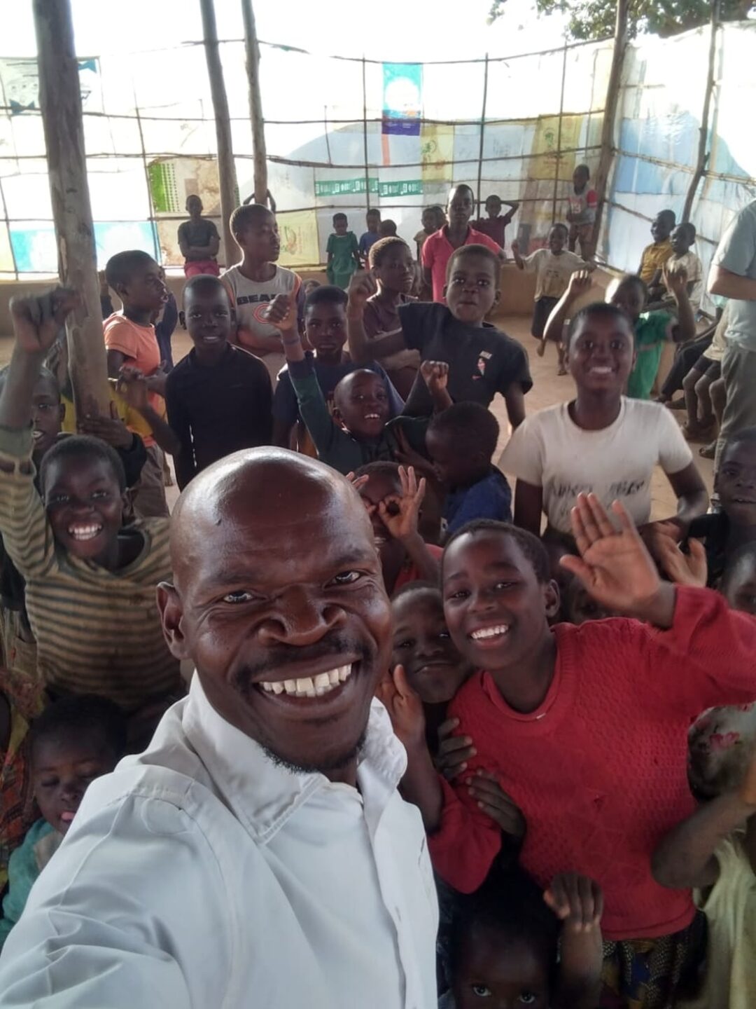 A pastor smiling with a hall full of cheering children in a rural Malawi church where copies of The Prayer were shared