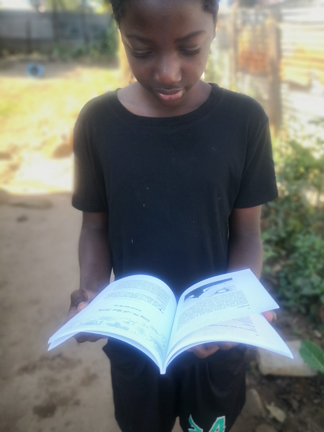 A young reader in Malawi holds an open copy of The Prayer, the pages catching the morning light