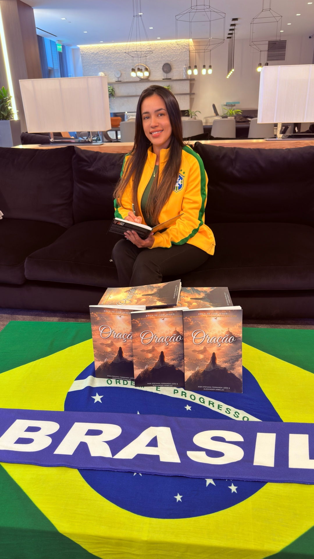 Stefania Leão in a Brazil jersey signs copies of Oração on the Brazil flag at Miami Hard Rock Stadium