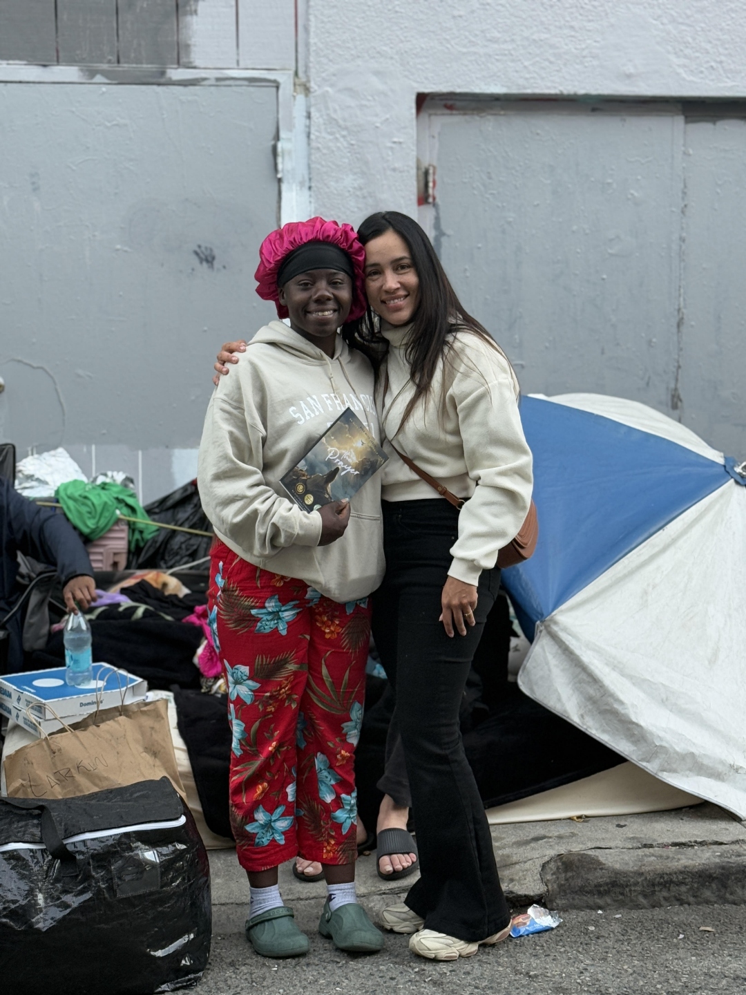 Stefania hugs a neighbor holding a copy of the prayer book in the SF Tenderloin