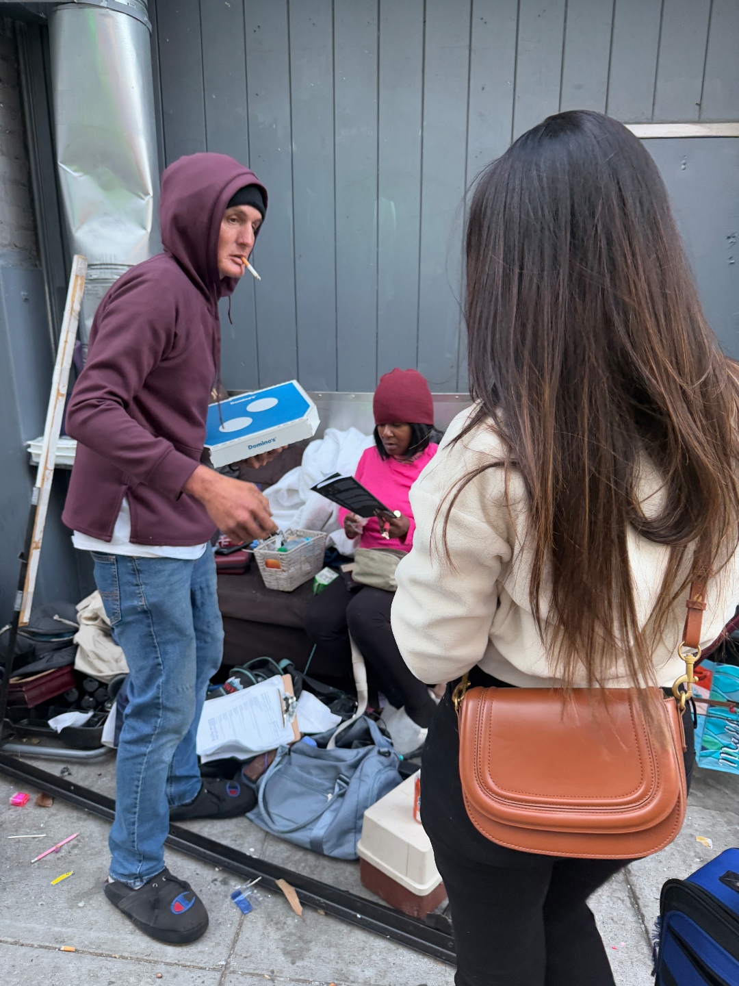 A neighbor in pink reads the prayer book on the sidewalk during the outreach drive
