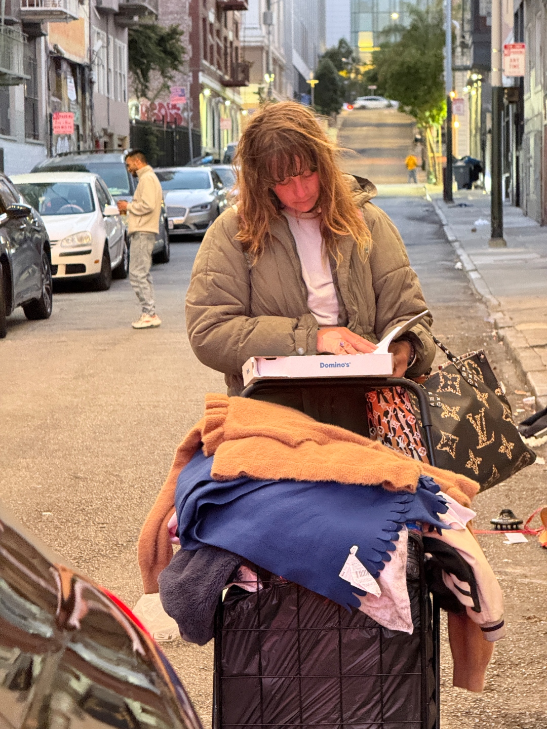 A neighbor in the SF Tenderloin reads a copy of the prayer book beside her belongings