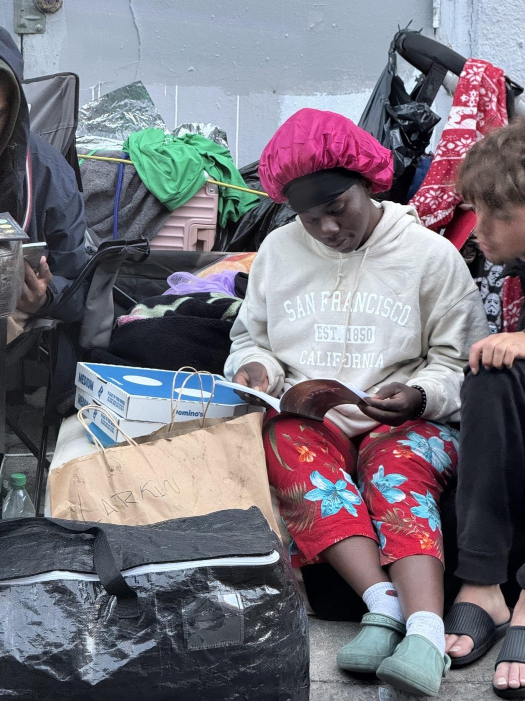 A woman in a San Francisco sweatshirt reads a copy of the prayer book on the sidewalk during the Tenderloin giveaway