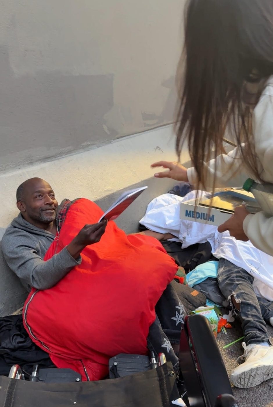 A man reads a copy of the prayer book while Stefania hands out books and food during the Tenderloin giveaway