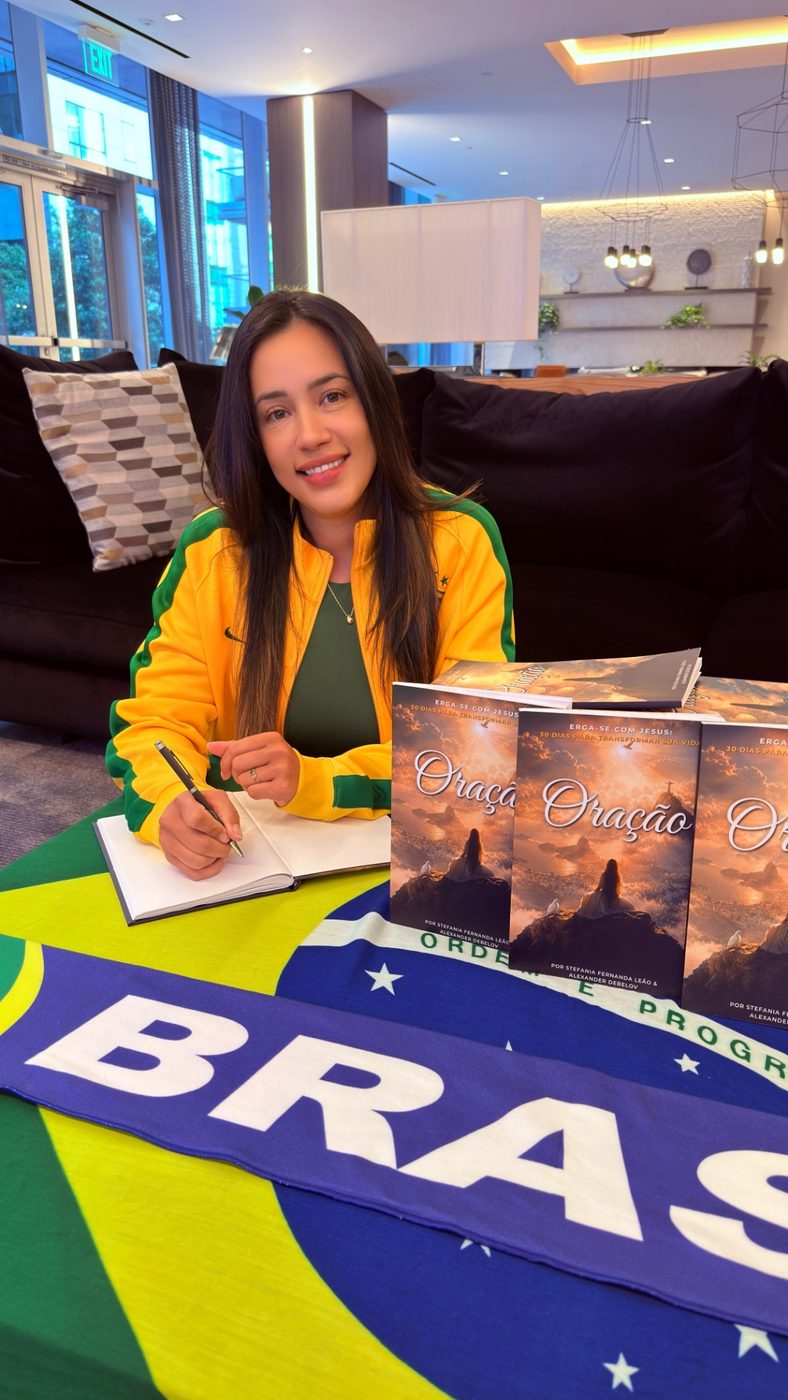 Close view of Alexander Debelov signing Oração books arranged on a Brazil flag tablecloth.