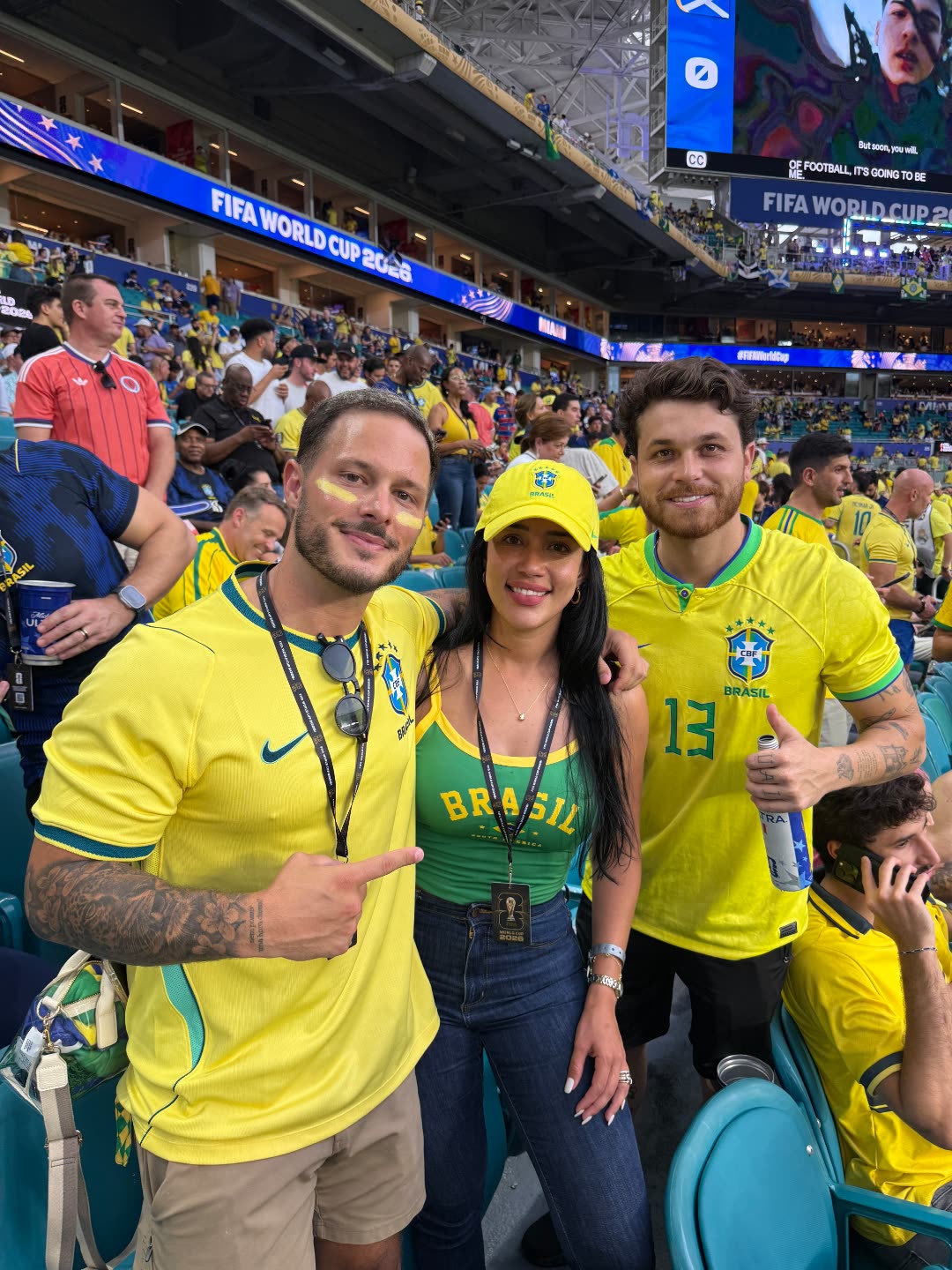 Stefania Le&atilde;o with Brazilian creators Joshua Canup (@gringocomedia) and Gustavo Tubar&atilde;o (@ogustavotubarao) in Brazil kits inside the stadium under the FIFA World Cup 2026 signage in Miami